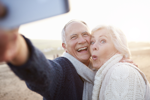 Senior Couple Standing On Beach Taking Selfie