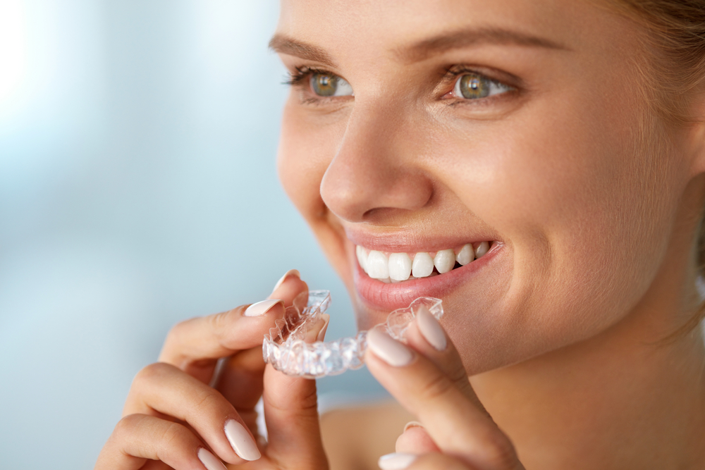 woman putting a clear aligner tray onto her teeth