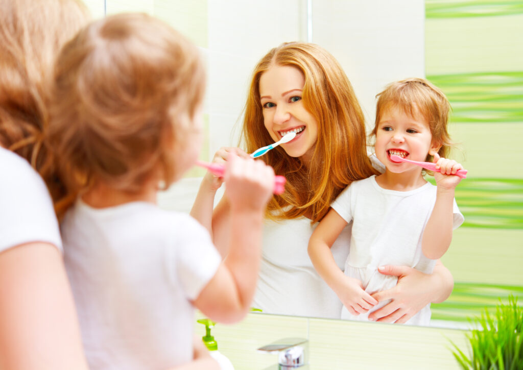 Parent and child brushing teeth together. 