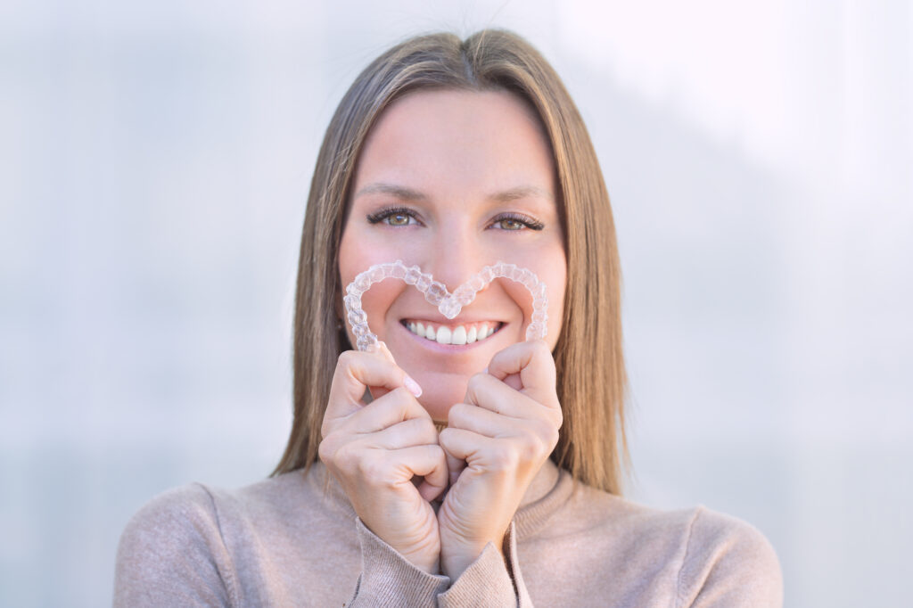 Woman with healthy teeth and gums holding Invisalign clear aligners.