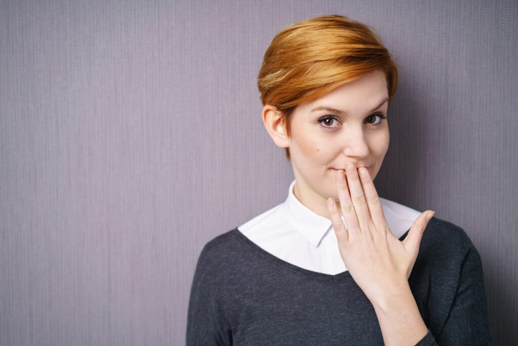 Young woman covering gums and teeth with her hand. 