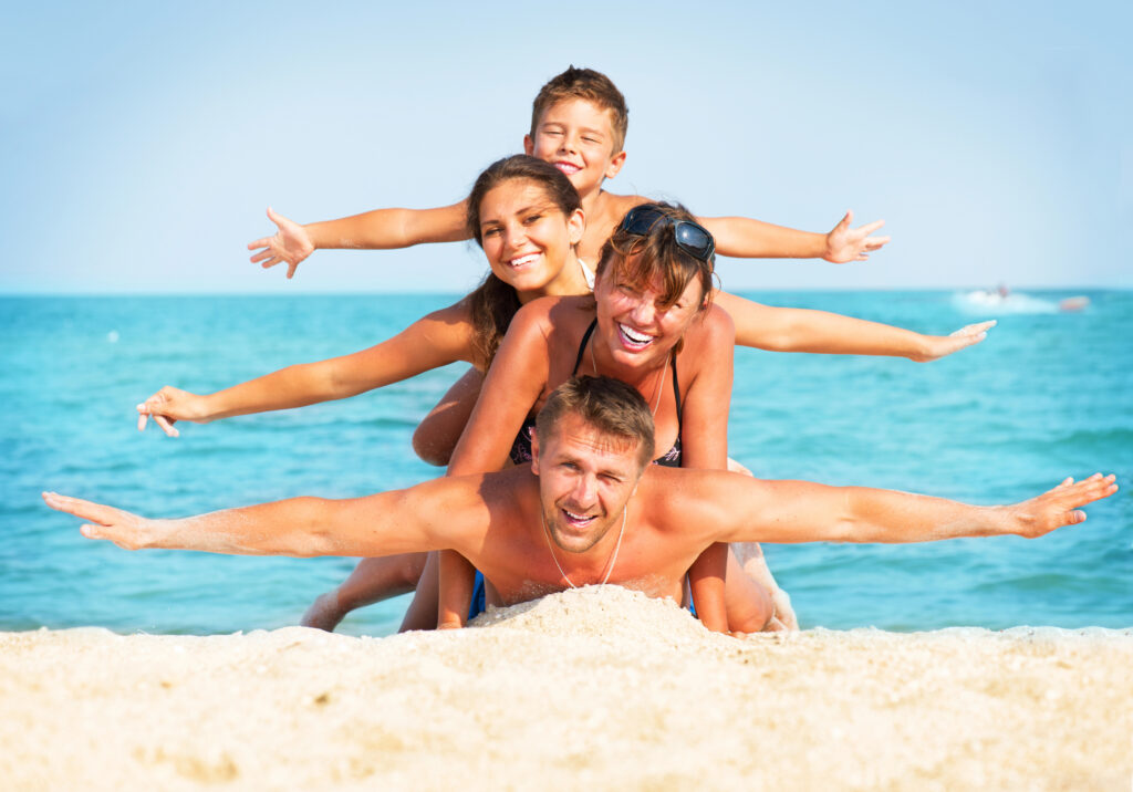 Family with healthy white smiles having fun at the beach in summer heat.